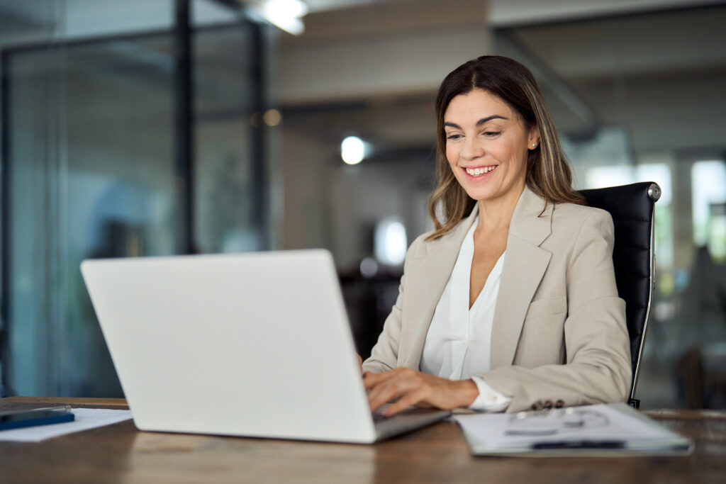 Happy mature professional business woman looking at laptop working in office.
